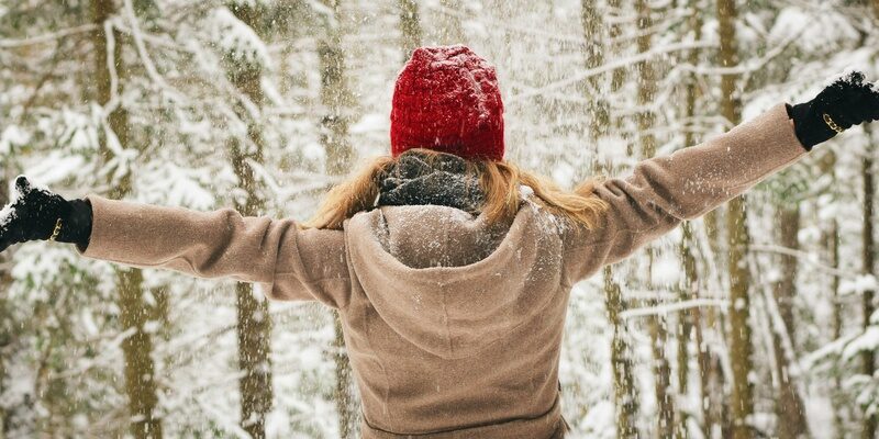 Woman in a beige winter coat and red bobble hat with arms outstretched in snowy woodland scene representing new year, and a new start, possibly divorce.