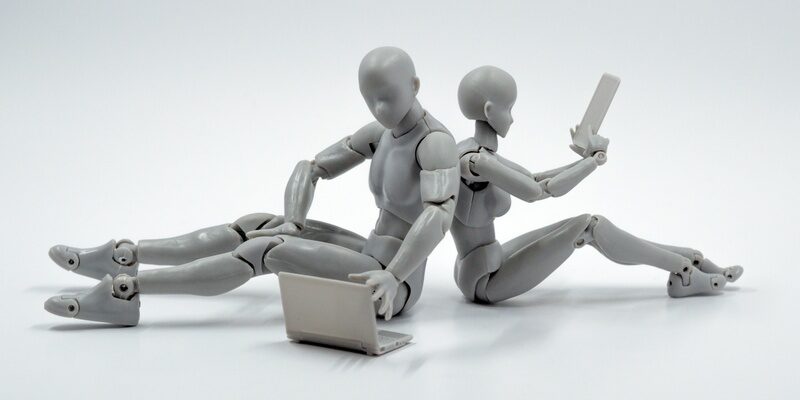 Male and Female grey model robots sat back to back with laptop and tablet indicating artificial intelligence (AI).
