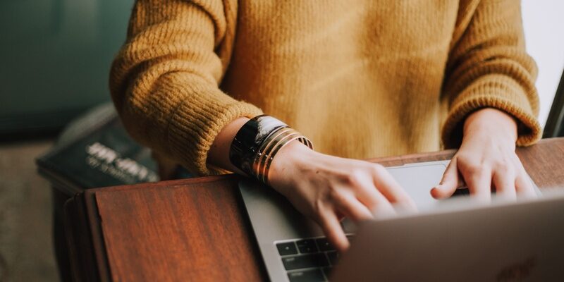 Woman in an orange jumper working at a laptop indicating questions about what is employment status?