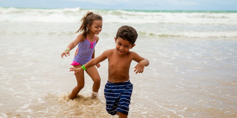 A boy and a girl paddle at the shoreline in beachwear representing the angle of the article about taking children abroad if you are separated.