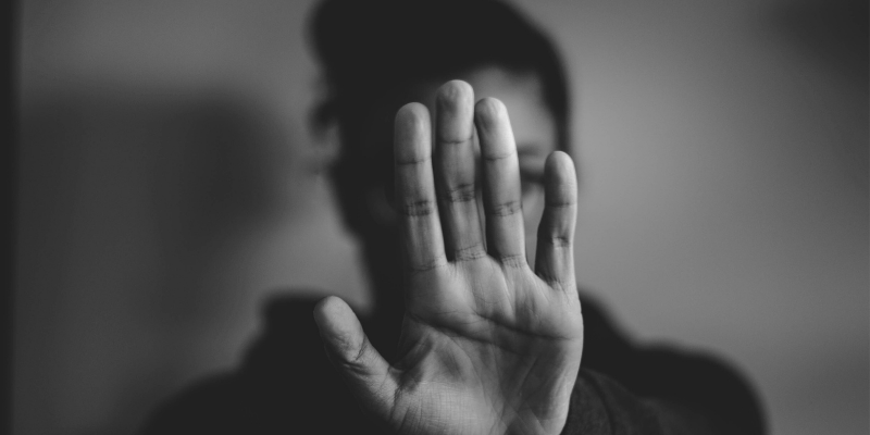 Black and white image of a woman with her hand in front of her face in a stop sign, signifying domestic abuse.